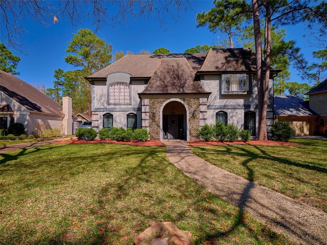 french country home with stucco siding, brick siding, and a front lawn