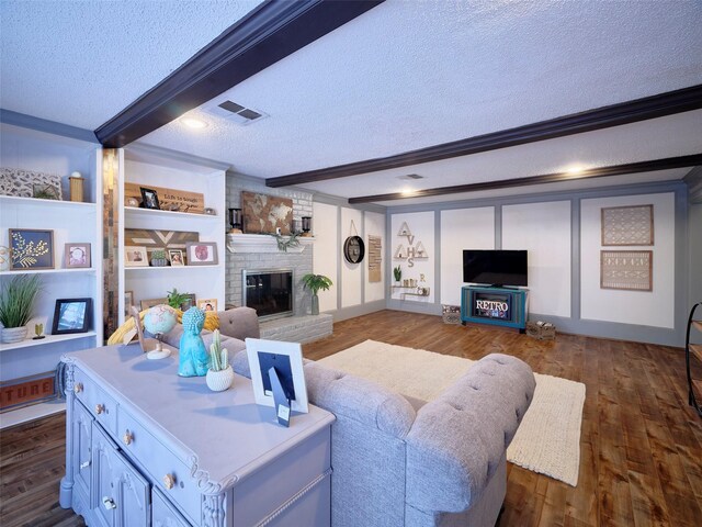 living room with beam ceiling, a textured ceiling, a brick fireplace, and dark wood finished floors