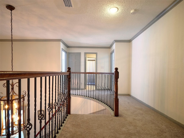 corridor featuring visible vents, a textured ceiling, carpet, crown molding, and baseboards