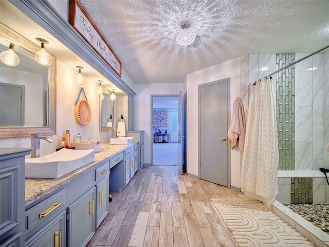 full bath with a sink, a textured ceiling, wood finished floors, a tile shower, and double vanity