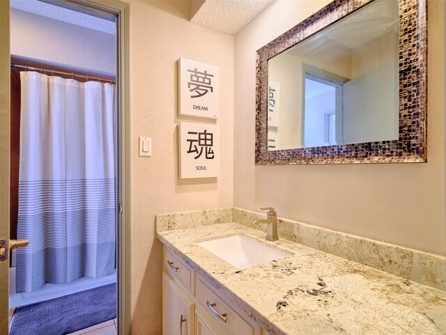 full bath with curtained shower, vanity, and a textured wall