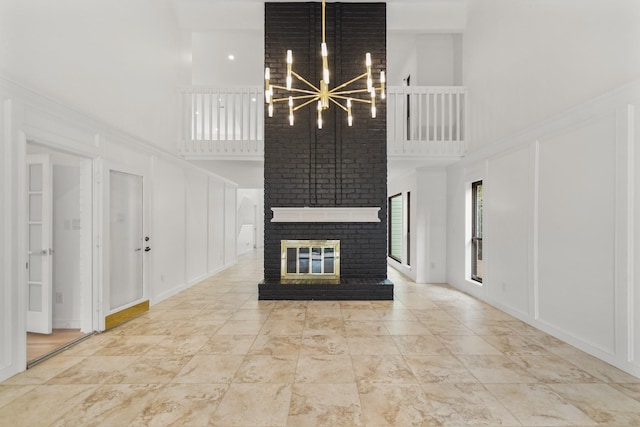 unfurnished living room featuring an inviting chandelier, a towering ceiling, a fireplace, and a decorative wall