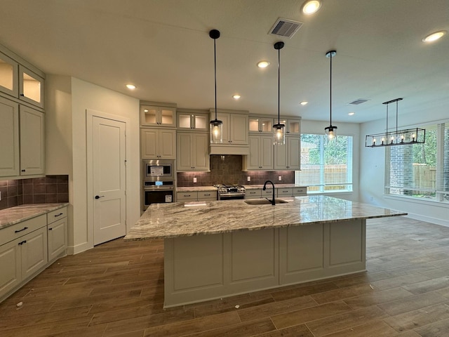 16174 Rustling Woods Rd, Conroe, TX 77302 - kitchen with appliances with stainless steel finishes, a sink, dark wood-type flooring, a center island with sink, and tasteful backsplash