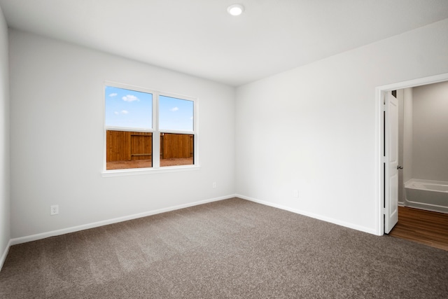 empty room featuring dark colored carpet and baseboards