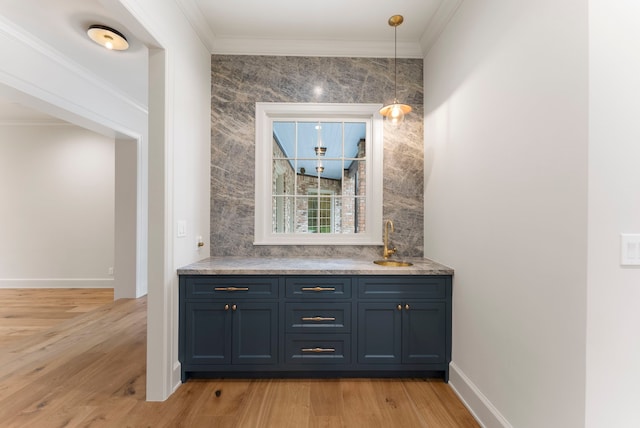 bar with baseboards, a sink, ornamental molding, light wood-style floors, and pendant lighting