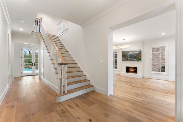 staircase featuring french doors, wood-type flooring, a warm lit fireplace, and ornamental molding