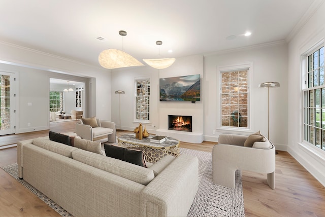 living room featuring visible vents, light wood-style flooring, a lit fireplace, crown molding, and baseboards