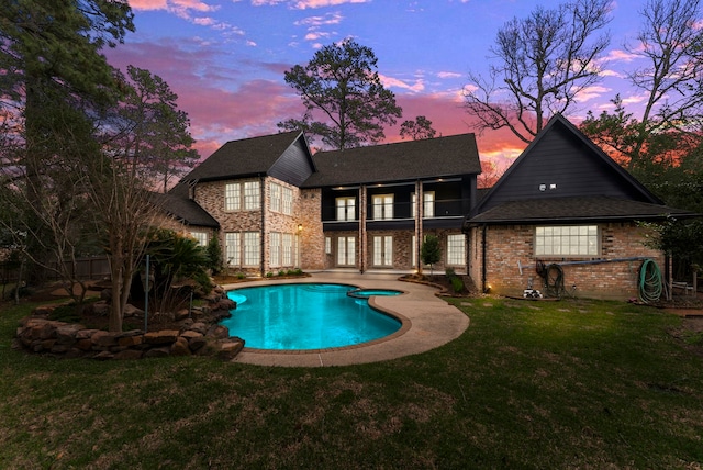 back of house at dusk featuring a lawn, a patio, a balcony, a fenced in pool, and brick siding