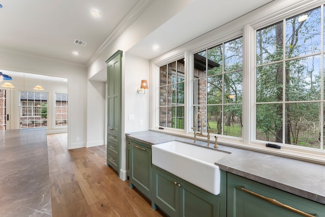 kitchen featuring visible vents, light wood-type flooring, a sink, crown molding, and green cabinetry