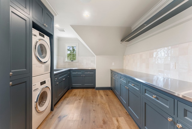 clothes washing area featuring light wood-type flooring, visible vents, stacked washer and clothes dryer, ornamental molding, and cabinet space