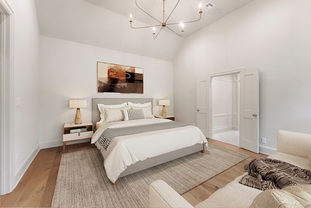 bedroom with light wood finished floors, visible vents, baseboards, vaulted ceiling, and an inviting chandelier