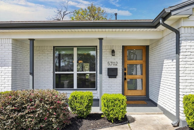 view of exterior entry featuring brick siding and a porch