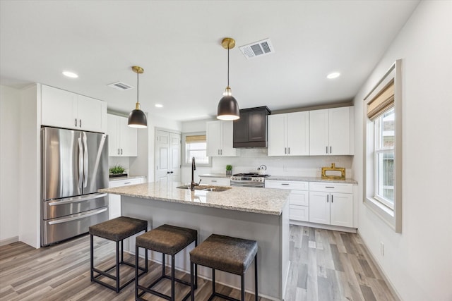 kitchen with visible vents, light wood-type flooring, decorative backsplash, stainless steel appliances, and a sink