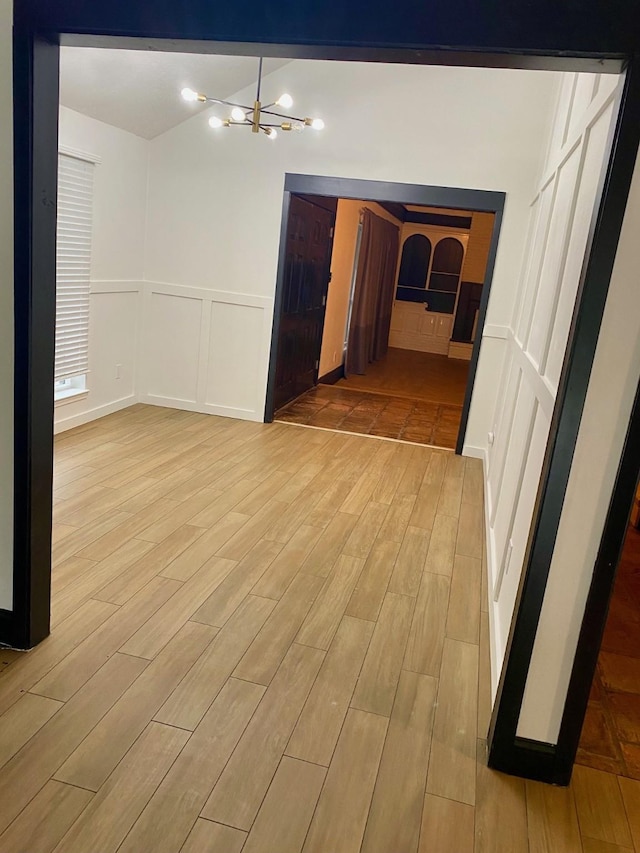 spare room featuring light wood-style flooring, vaulted ceiling, wainscoting, a decorative wall, and a chandelier