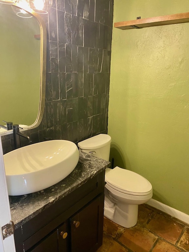 bathroom with toilet, vanity, tile walls, and baseboards