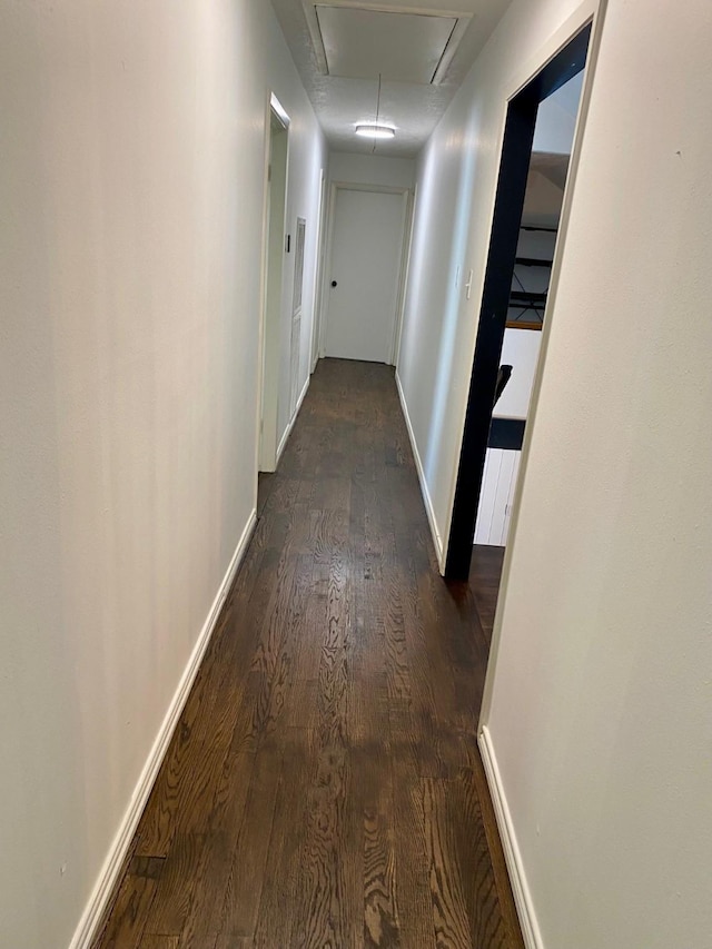 hall featuring dark wood finished floors, attic access, and baseboards