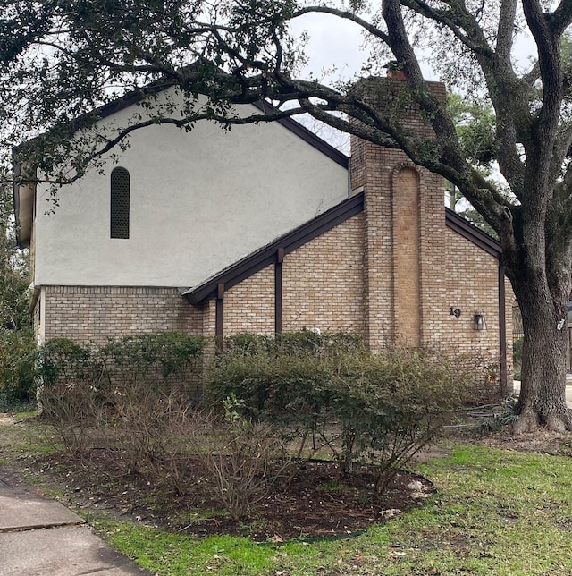 view of side of property featuring stucco siding, brick siding, and a chimney