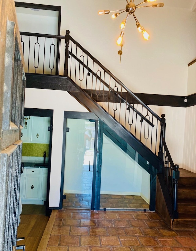 stairs with a chandelier, brick floor, and a towering ceiling