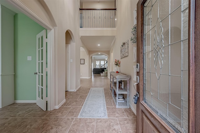 entryway featuring arched walkways, baseboards, and a towering ceiling