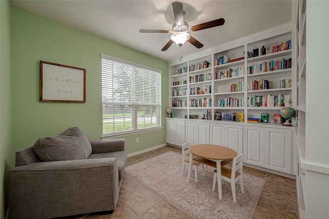 living area featuring baseboards, built in shelves, and a ceiling fan