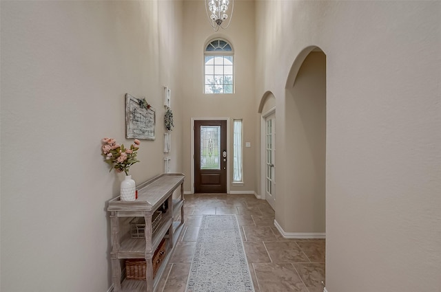 foyer entrance with a notable chandelier, stone tile floors, arched walkways, a high ceiling, and baseboards