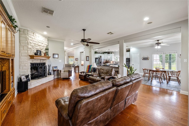 living area with a fireplace, visible vents, wood-type flooring, and ornamental molding