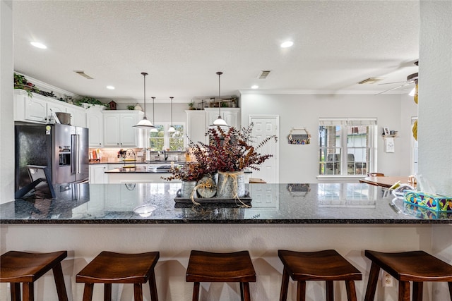 kitchen with visible vents, a breakfast bar, a peninsula, high end fridge, and white cabinetry