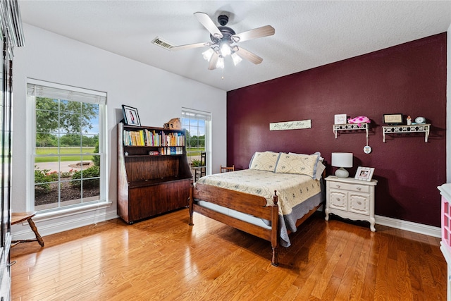 bedroom featuring ceiling fan, visible vents, baseboards, and hardwood / wood-style floors