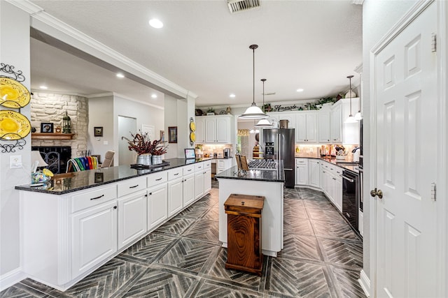 kitchen with visible vents, a stone fireplace, white cabinets, stainless steel fridge, and backsplash