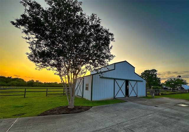 outdoor structure at dusk with an outbuilding, a barn, a lawn, and fence