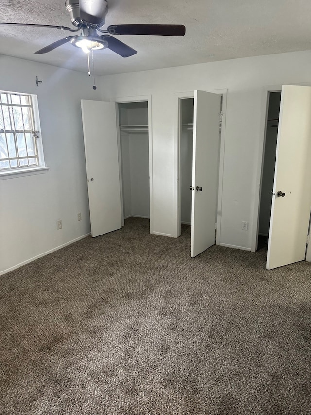 unfurnished bedroom featuring carpet, baseboards, ceiling fan, a textured ceiling, and two closets