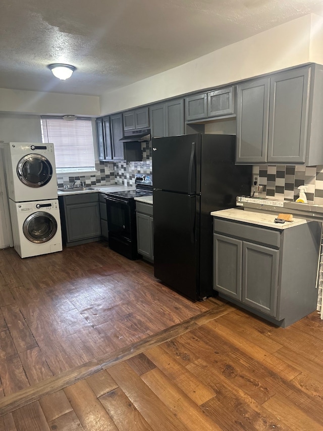 kitchen featuring gray cabinets, black appliances, dark wood-type flooring, stacked washer / drying machine, and backsplash