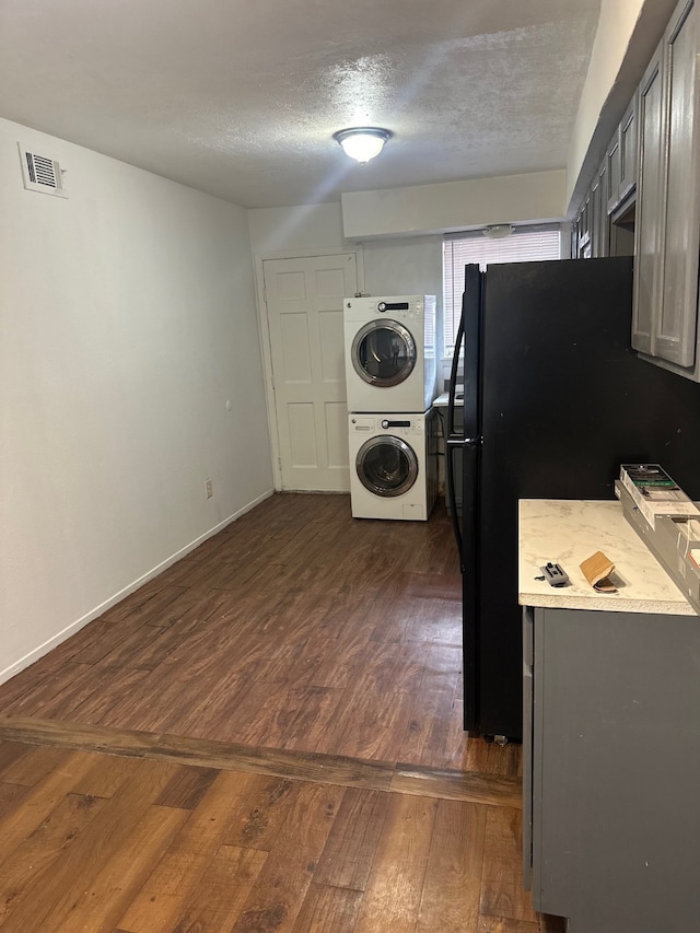 laundry room featuring baseboards, visible vents, stacked washing maching and dryer, dark wood finished floors, and a textured ceiling