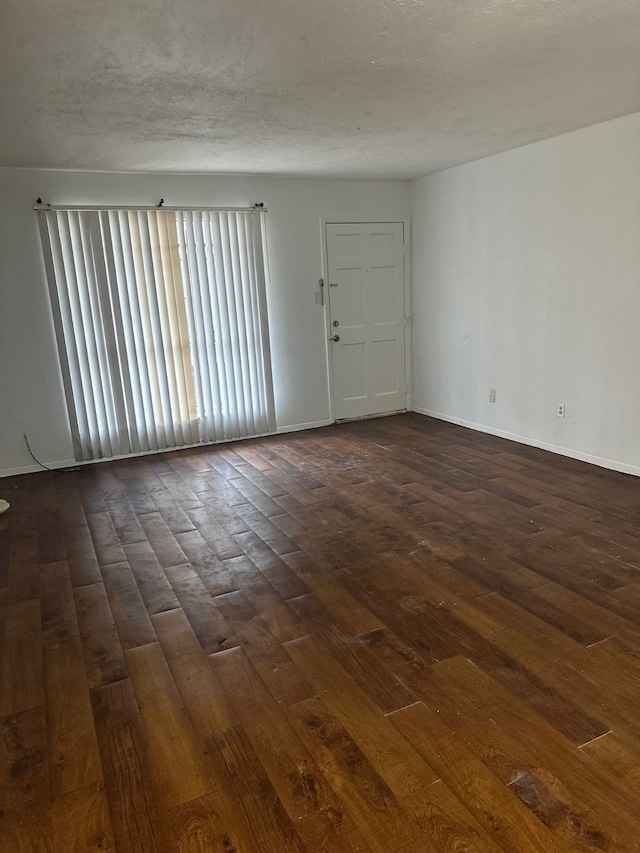 spare room with dark wood finished floors, a textured ceiling, and baseboards