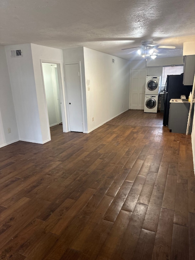 unfurnished living room featuring visible vents, dark wood-type flooring, stacked washer and clothes dryer, a ceiling fan, and a textured ceiling