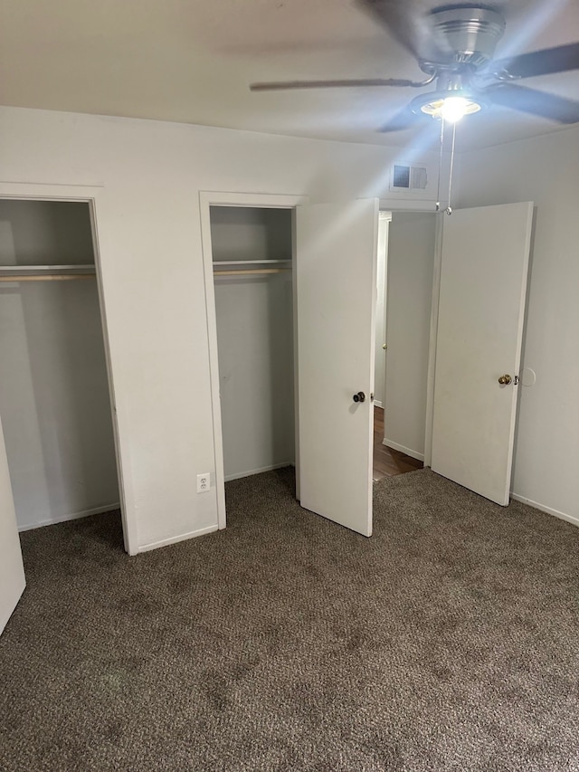 unfurnished bedroom with visible vents, two closets, and dark carpet