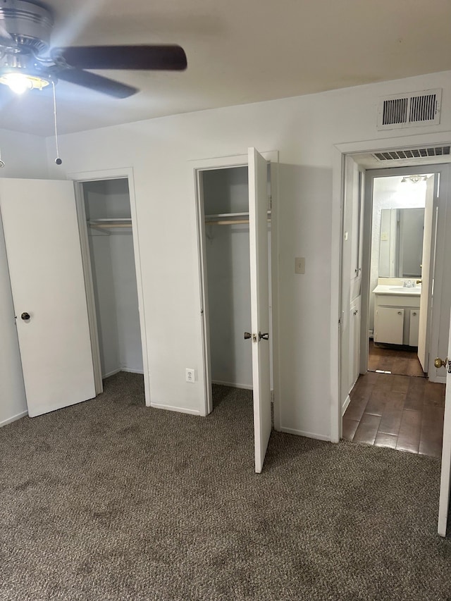 unfurnished bedroom with dark colored carpet, visible vents, two closets, and a ceiling fan