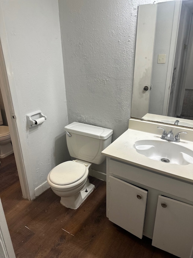 half bath with vanity, wood finished floors, toilet, and a textured wall