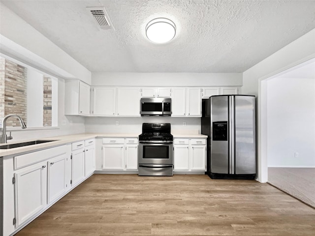 kitchen featuring visible vents, light wood-type flooring, appliances with stainless steel finishes, white cabinetry, and a sink