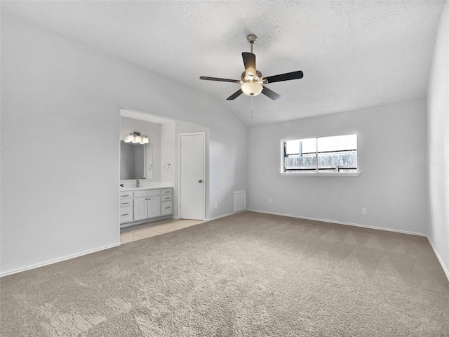 unfurnished bedroom with baseboards, lofted ceiling, a textured ceiling, light colored carpet, and connected bathroom