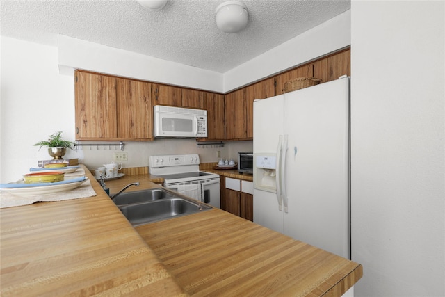 kitchen featuring a sink, a textured ceiling, white appliances, brown cabinetry, and light countertops