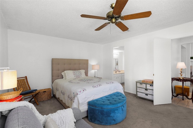 bedroom featuring a textured ceiling, ensuite bathroom, carpet, and a ceiling fan