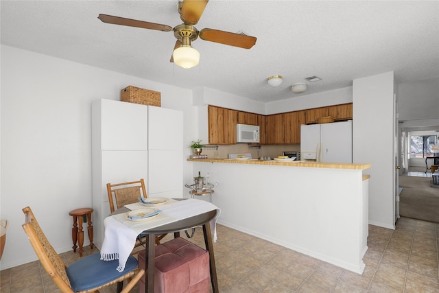 kitchen featuring visible vents, brown cabinets, a textured ceiling, white appliances, and a peninsula