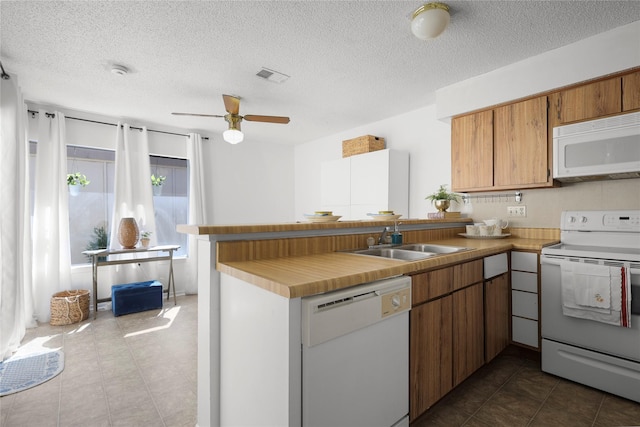 kitchen featuring visible vents, brown cabinets, a peninsula, white appliances, and a sink