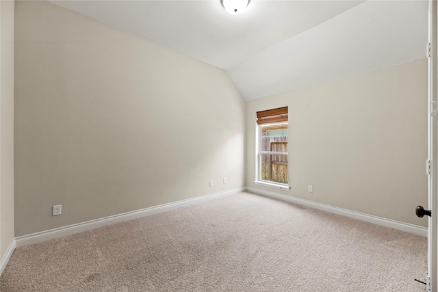 carpeted spare room featuring lofted ceiling and baseboards