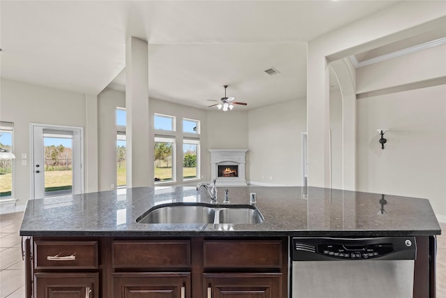 kitchen with dark stone countertops, a lit fireplace, a sink, dark brown cabinetry, and stainless steel dishwasher