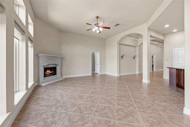 unfurnished living room featuring visible vents, baseboards, light tile patterned floors, a warm lit fireplace, and a ceiling fan