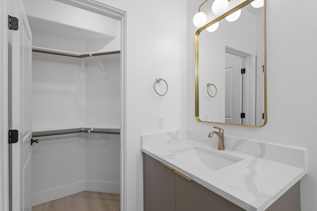 bathroom featuring vanity, a spacious closet, wood finished floors, and baseboards