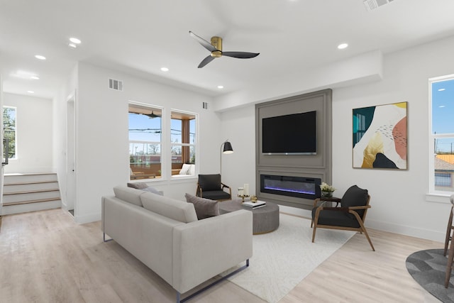 living room with light wood finished floors, visible vents, baseboards, recessed lighting, and a glass covered fireplace