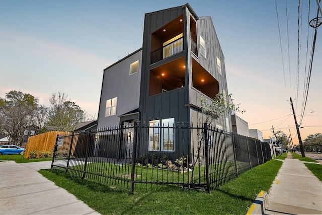 property exterior at dusk with a fenced front yard, a lawn, and board and batten siding